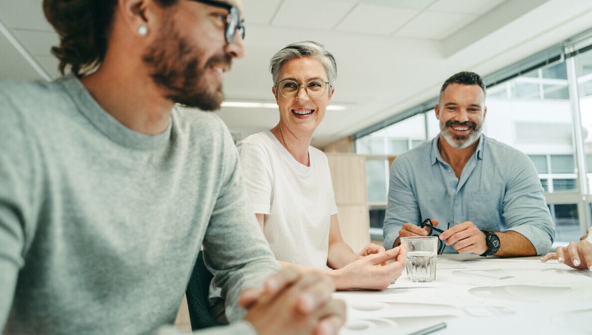 Kolleginnen und Kolleginnen diskutieren gutgelaunt am Besprechungstisch über ein Projekt.