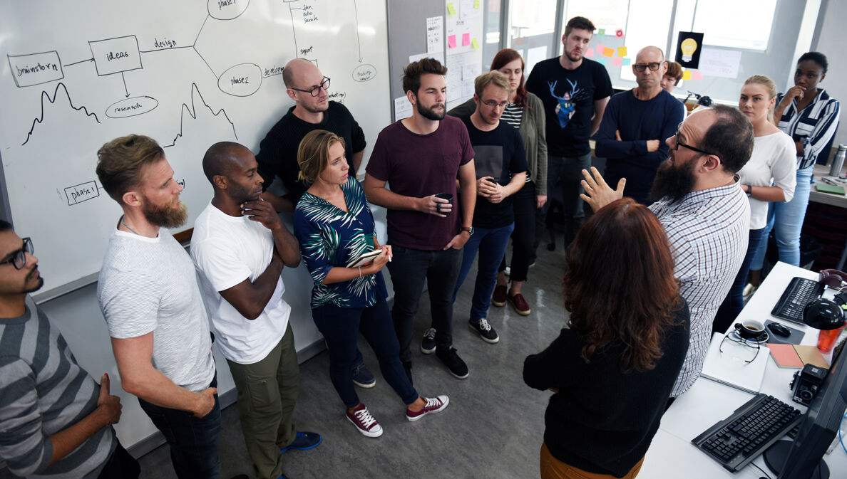 Ein diverses Business Team diskutiert miteinander vor einer Tafel.