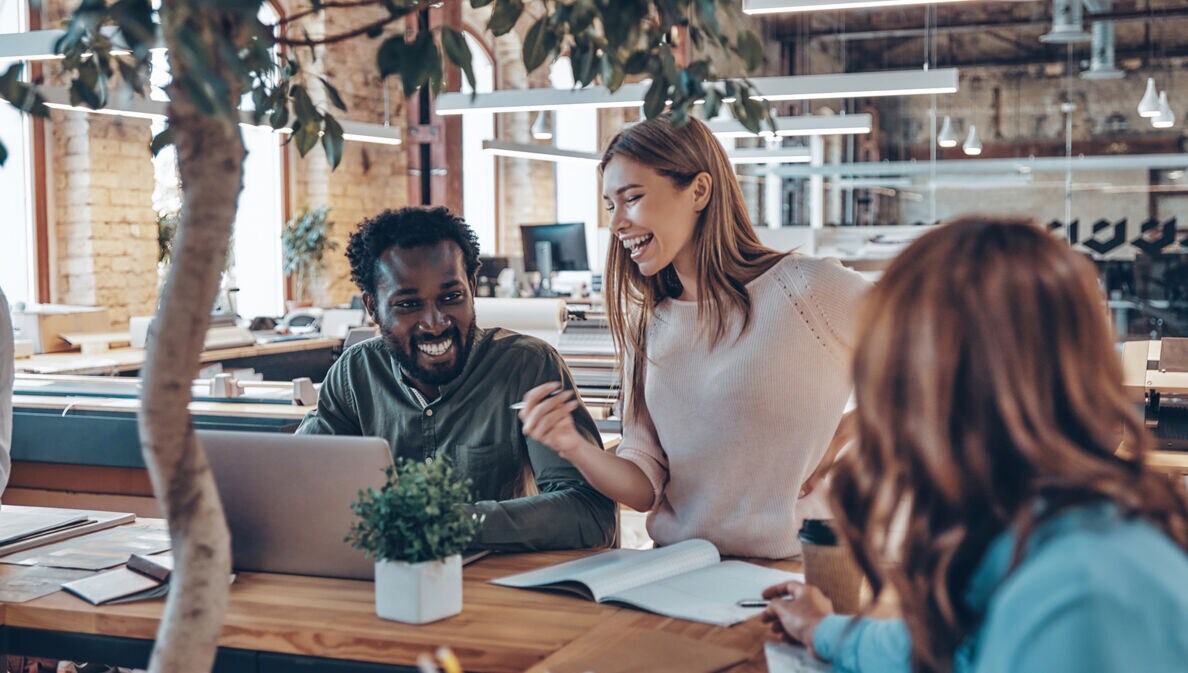 Drei junge Geschäftsleute unterhalten sich in einem hellen, modern eingerichteten Großraumbüro.