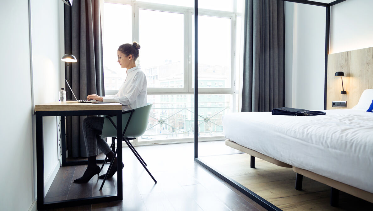 Eine junge Geschäftsfrau arbeitet am Laptop in ihrem Hotelzimmer.