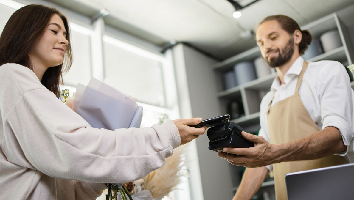 Eine junge Frau bezahlt mit ihrem Smartphone im Blumenladen.
