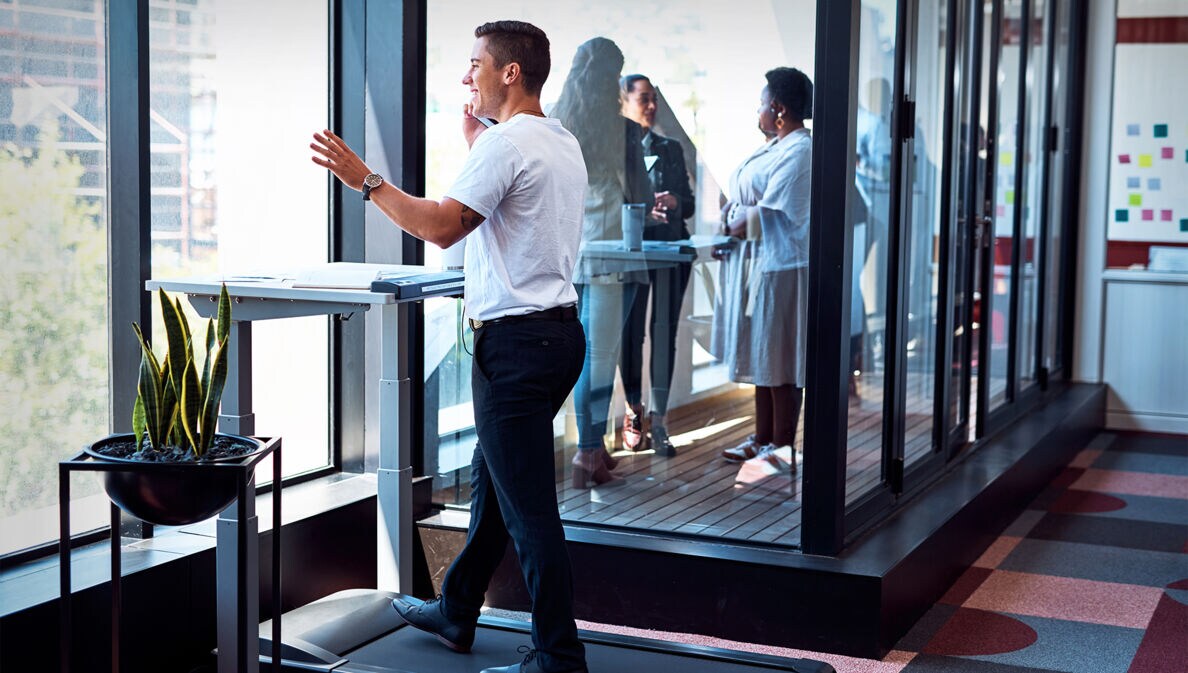 Ein Geschäftsmann trainiert im Büro auf einem Laufband und telefoniert dabei.