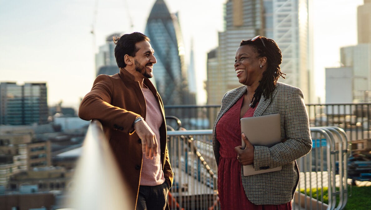 Eine Geschäftsfrau und ein Geschäftsmann unterhalten sich auf einer Dachterasse in London.