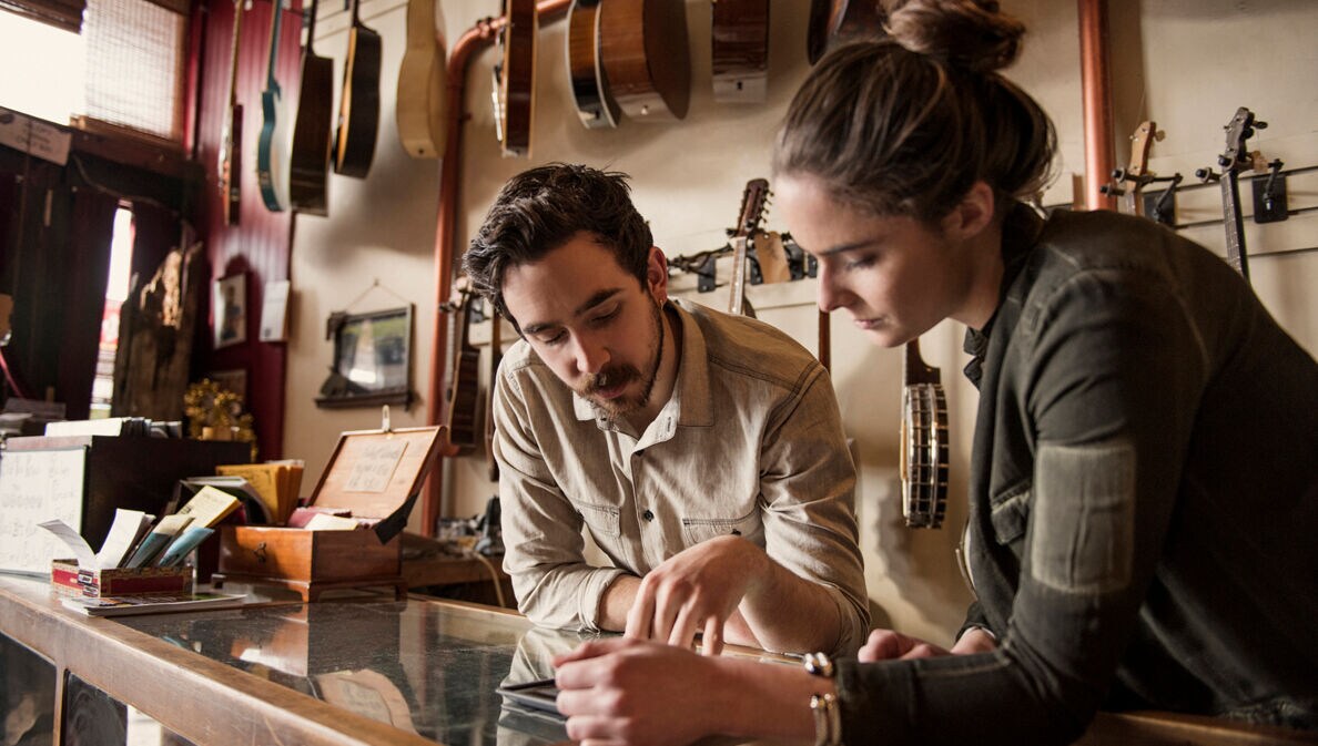Die Inhaberin und der Inhaber eines Gitarrenshops schauen gemeinsam auf einen Taschenrechner.