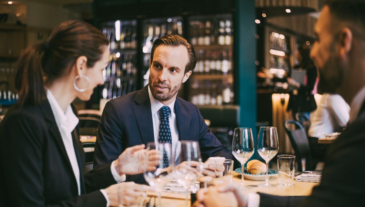 Mehrere Personen sitzen beim Business Lunch im gemütlichen italienischen Restaurant: Sie speisen und sind mitten im Small Talk.