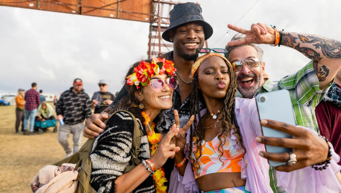 Freunde in bunten Festival-Outfits posieren für ein Selfie.