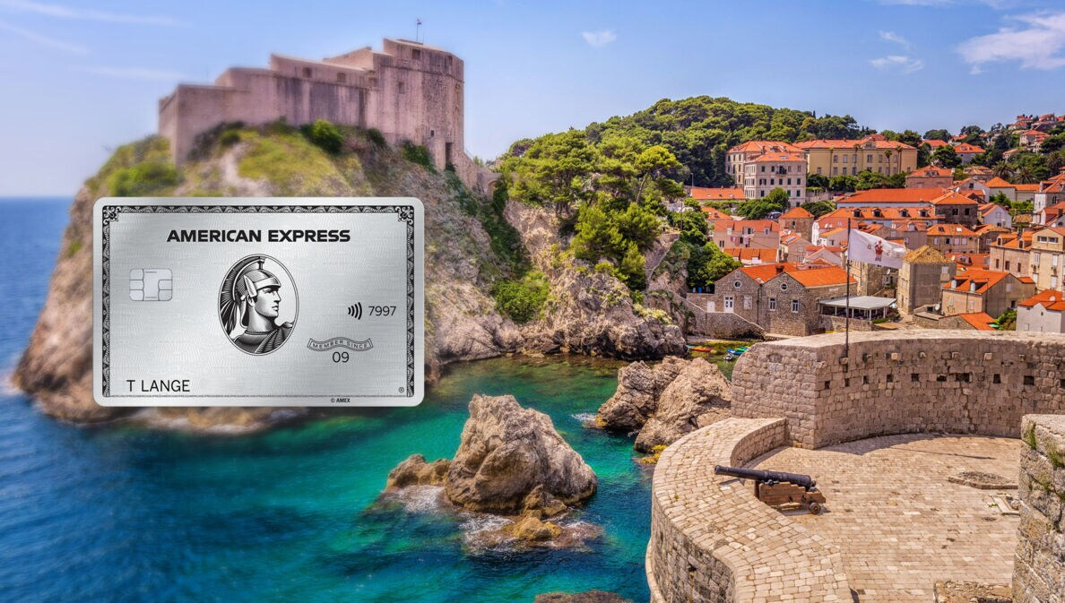 Ortschaft in einer Bucht mit türkisblauem Wasser an einer Felsküste mit historischen Festungen, im Vordergrund eine Aussichtsplattform mit Kanone auf einem Fort.