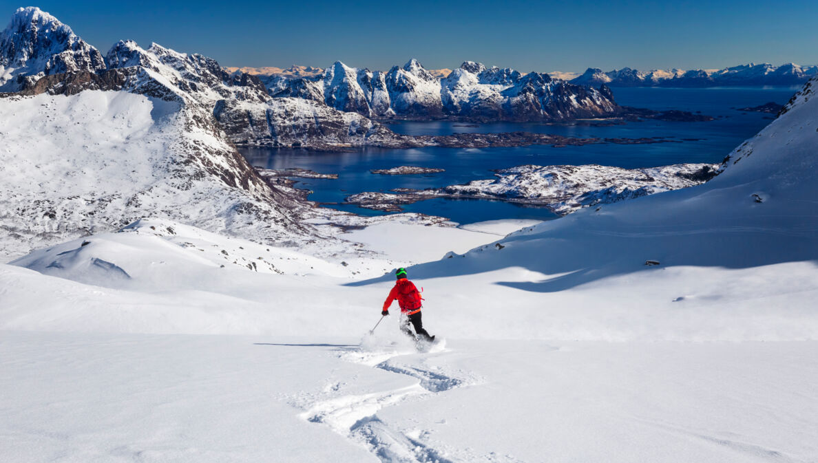 Person auf Skiern, im Hintergrund Berge und Wasser.