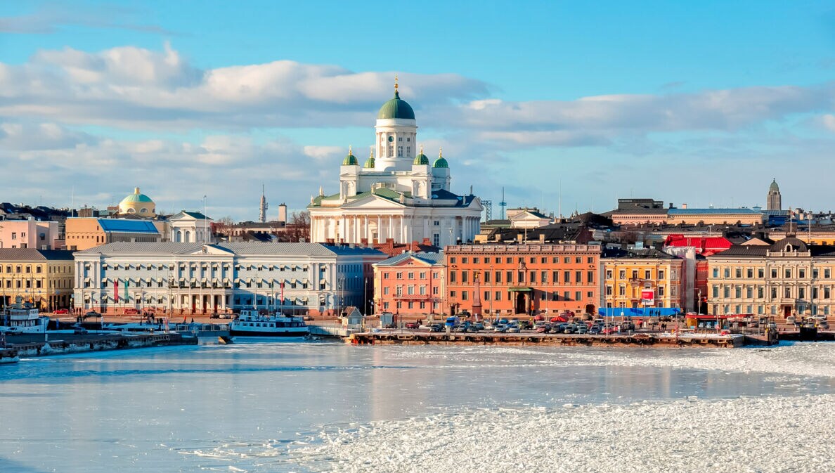 Stadtpanorama von Helsinki mit Dom an einer zugefrorenen Wasserfläche im Vordergrund.