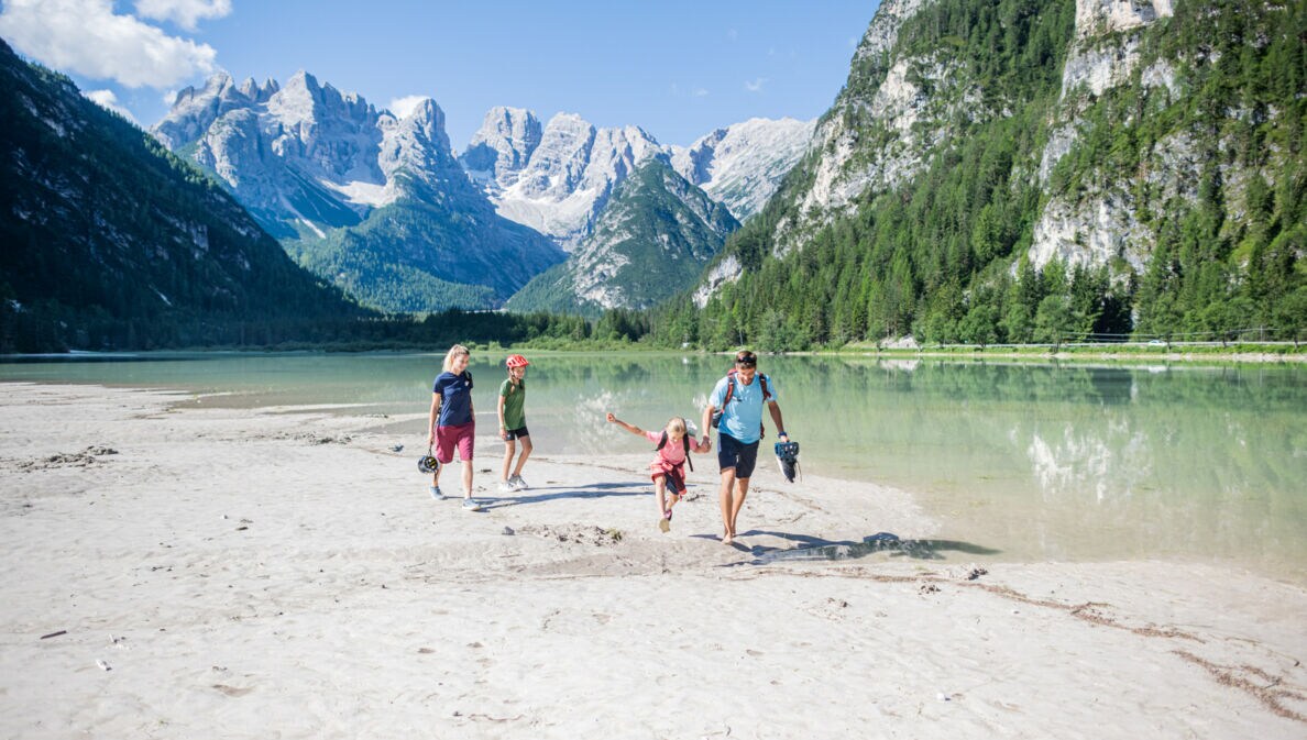 Eine Familie mit zwei Kindern in sommerlicher Sportkleidung läuft an einem See in den Bergen entlang.