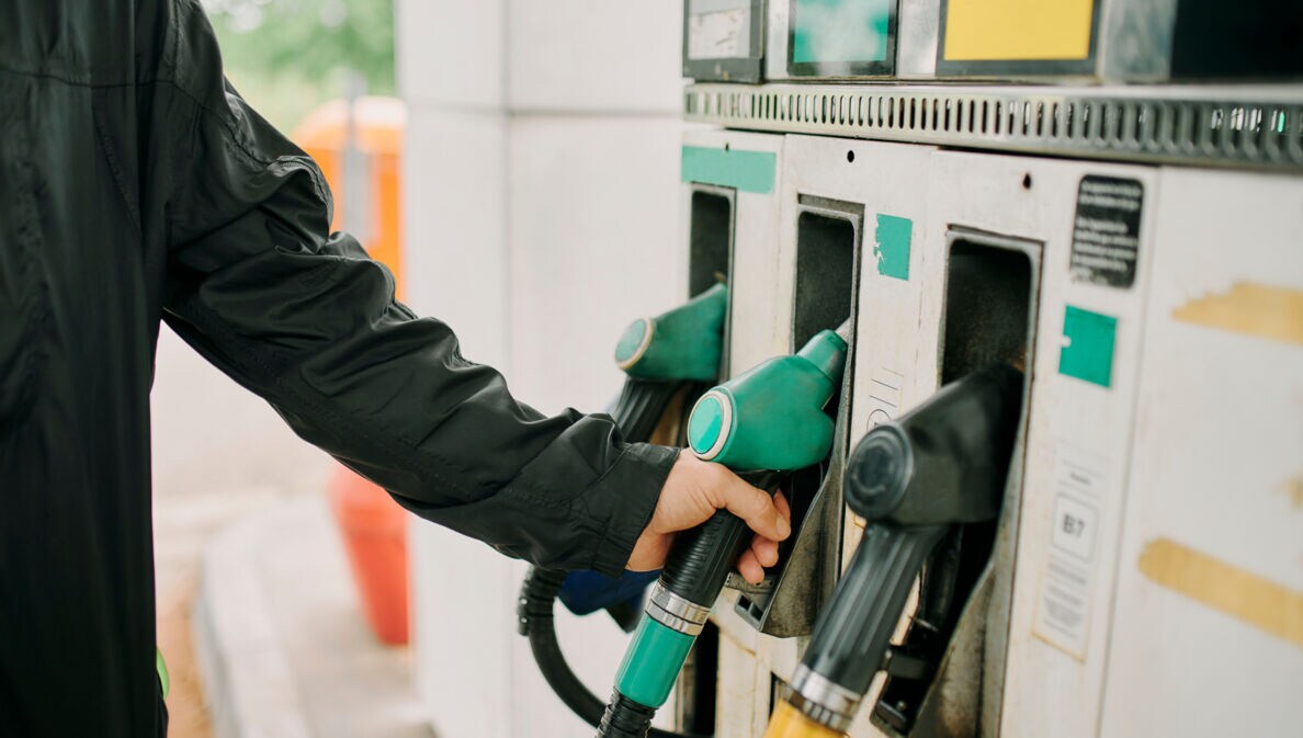 Close-up – Mann greift nach einem Zapfventil an einer Tankstelle.