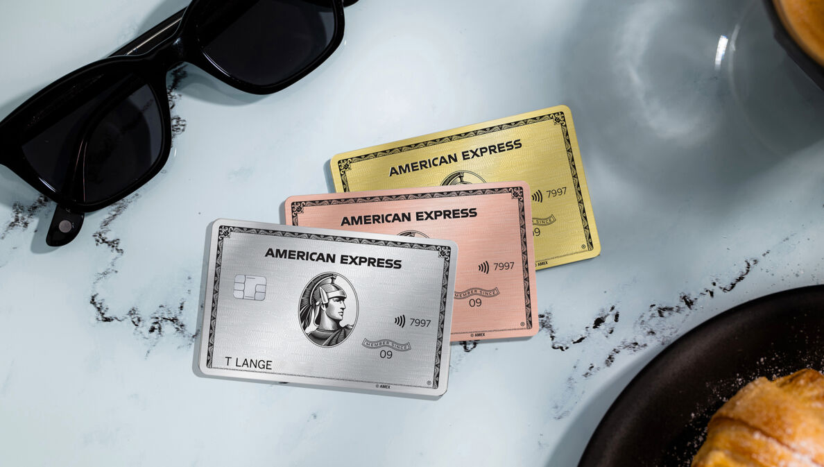 Drei Kreditkarten von American Express liegen auf einem Kaffeetisch aus Marmor, drum herum ist ein Croissants und eine Sonnenbrille.