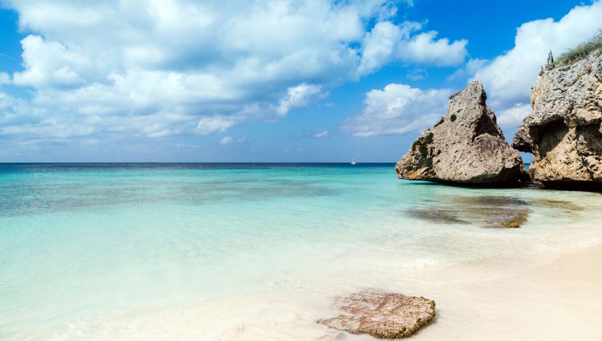 Weißer Strand am türkisblauen Meer, am Rand große Felsen im Wasser.