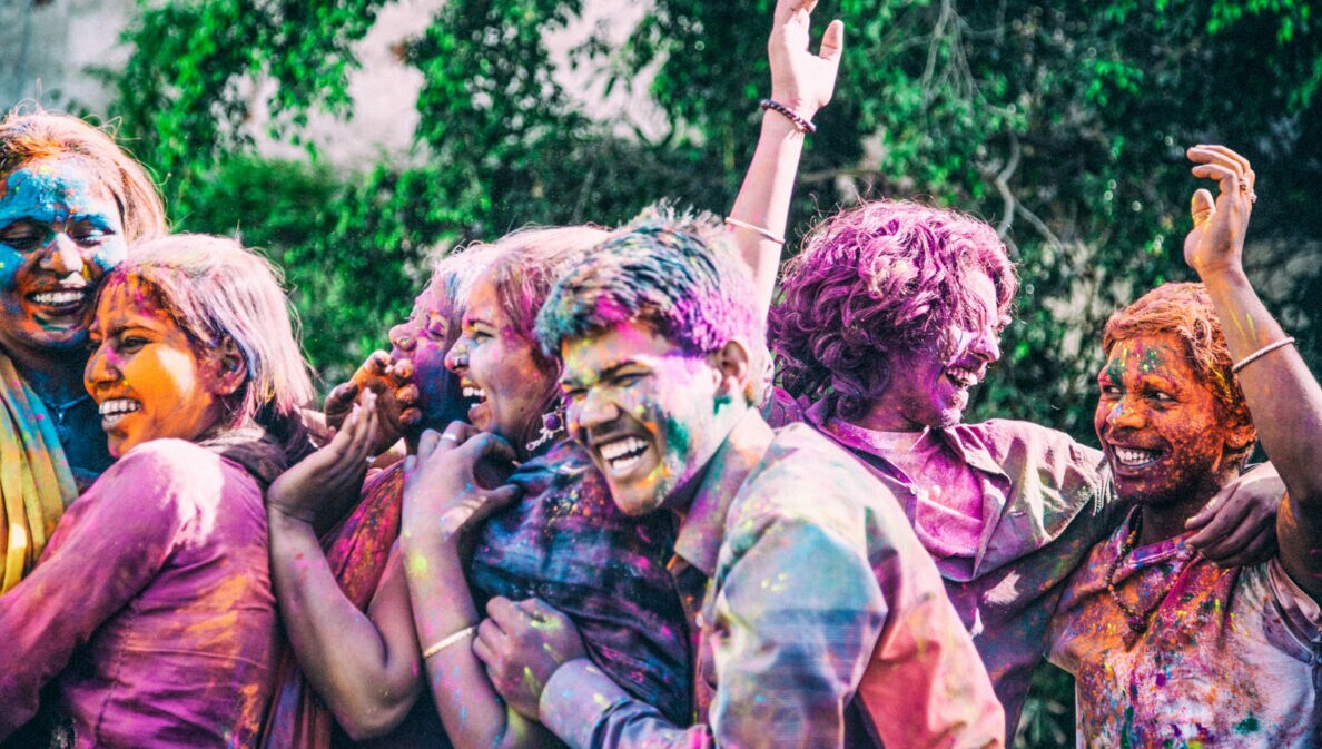 Lachende Personen indischer Abstammung voll mit bunter Farbe auf einem Holi Festival.