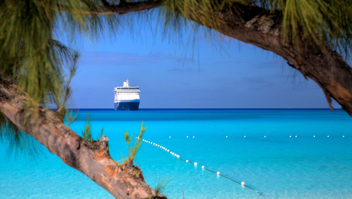 Kreuzfahrtschiff am Horizont eines Karibikstrands mit klarem türkisfarbenem Wasser.