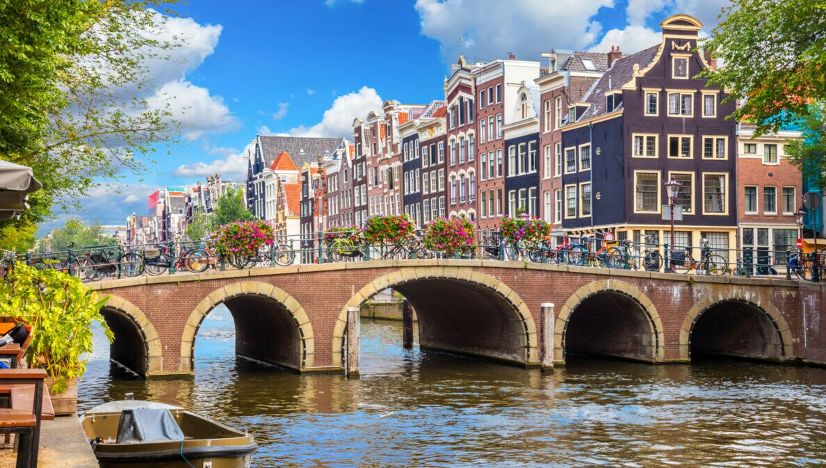 Eine mit Blumen geschmückte Steinbrücke über einem Kanal vor einer Reihe Grachtenhäuser im Stadtzentrum von Amsterdam.