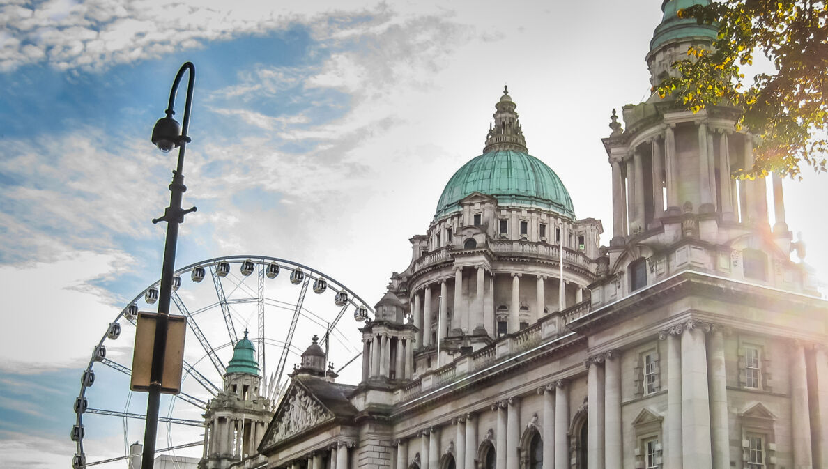 Historisches Gebäude mit grüner Kuppel und Riesenrad im Hintergrund bei Sonnenlicht