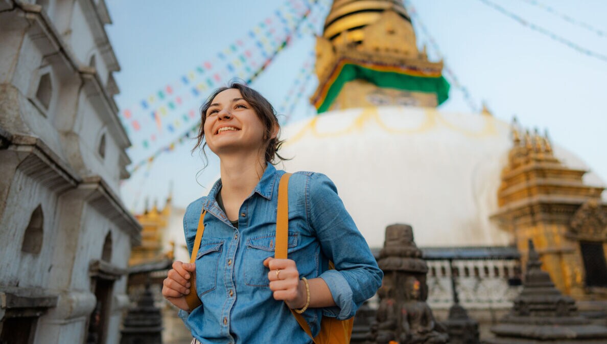 Eine junge, lächelnde Frau mit Rucksack vor einem nepalesischen Tempel.
