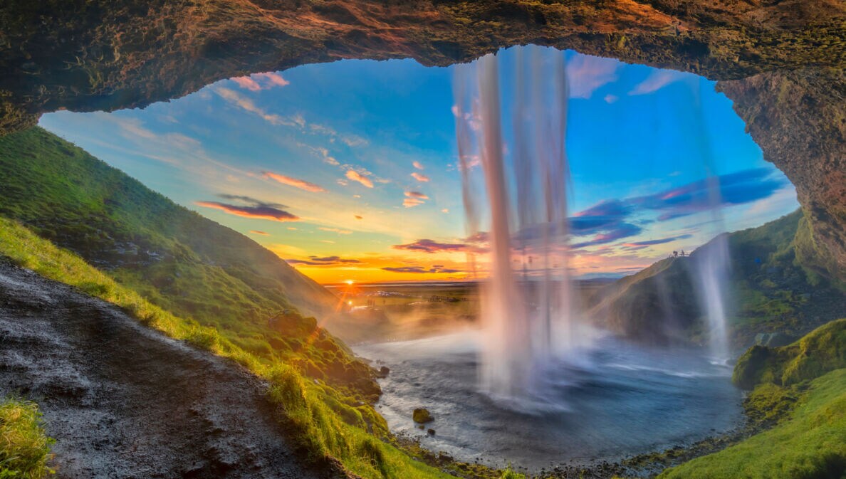 Wasserfall, der von einer Höhle aus bei Sonnenuntergang in eine grüne Landschaft fällt