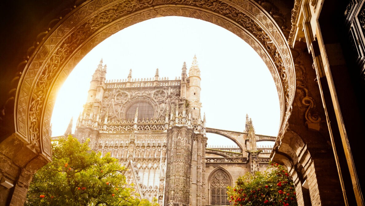 Gotische Kathedrale mit detaillierten Steinmetzarbeiten, gesehen durch einen verzierten Bogenrahmen bei Sonnenlicht