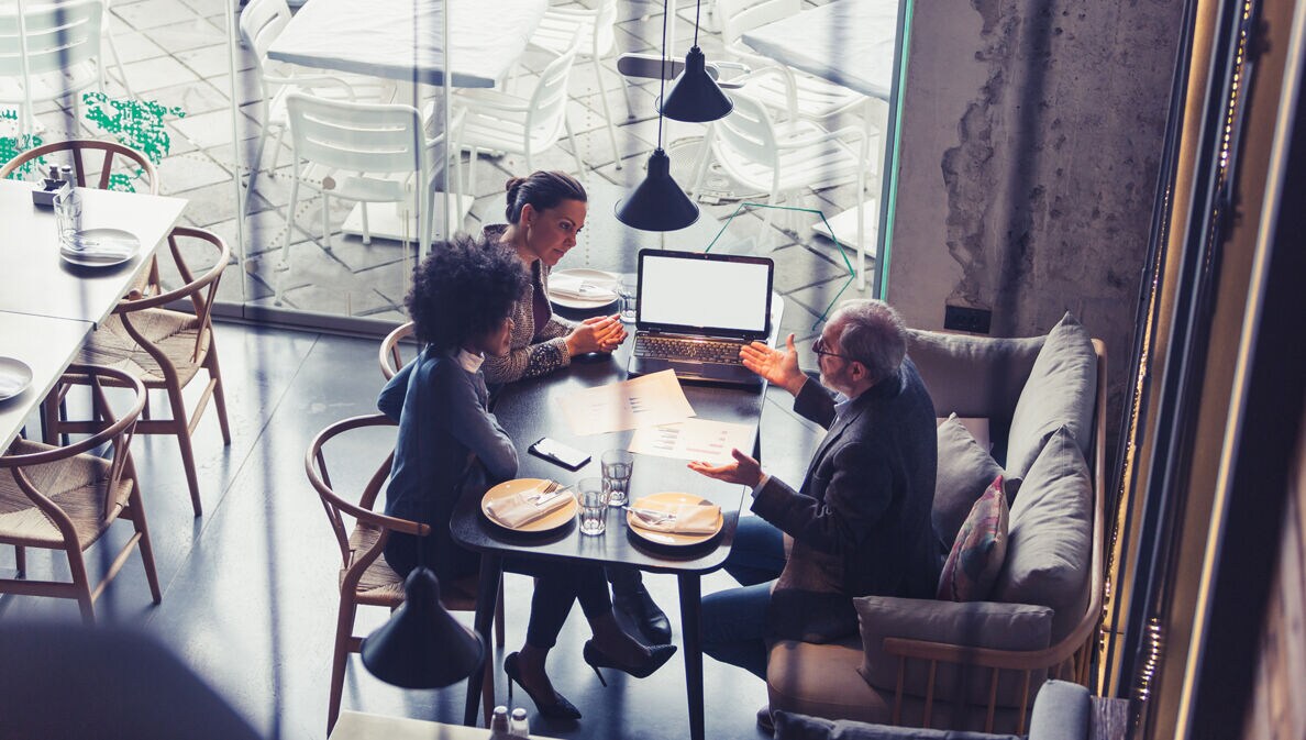 Mehrere Personen sitzen in einem Café für ein Arbeitsmeeting.