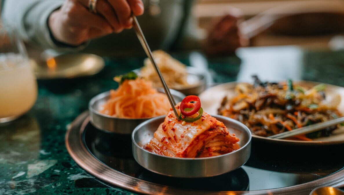 Eine Hand stippt Essstäbchen in eine Schale mit fermentiertem Kohl auf einem Tisch in einem Restaurant.