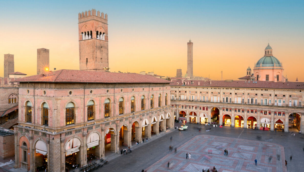Historische Gebäude mit Arkaden und Turm am Piazza Maggiore in Bologna bei Sonnenuntergang