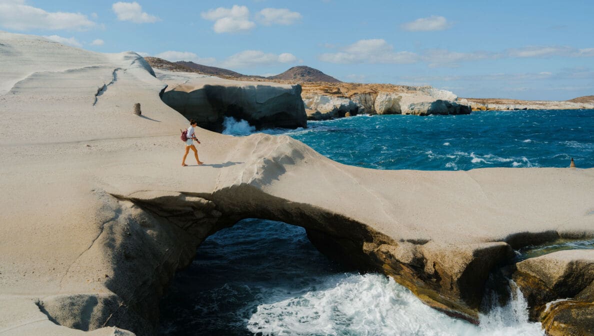 Eine Frau läuft auf einer bizarren Felsformation aus Vulkangestein am Meer.