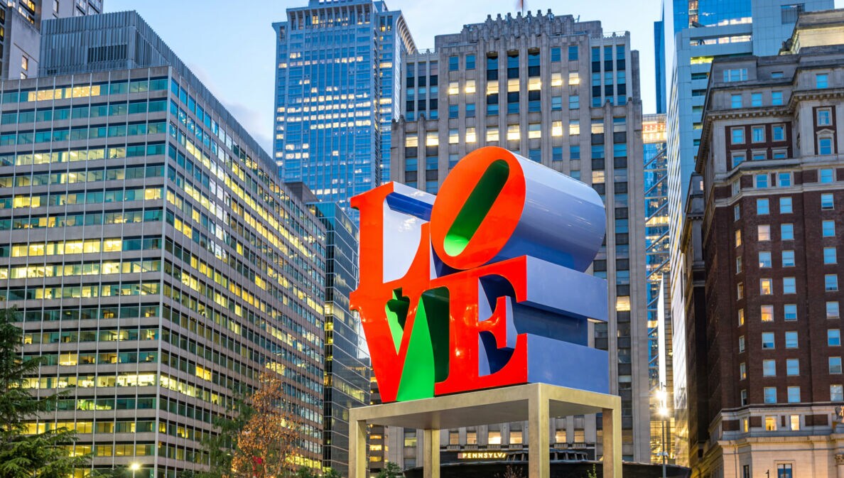 Skulptur mit dem Schriftzug 'LOVE' in roten und grünen Buchstaben vor Hochhäusern in einer Stadt