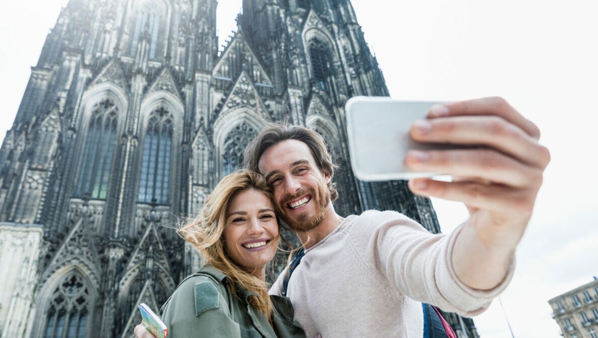 Junges Paar macht Selfie vor dem gotischen Kölner Dom an einem hellen Tag