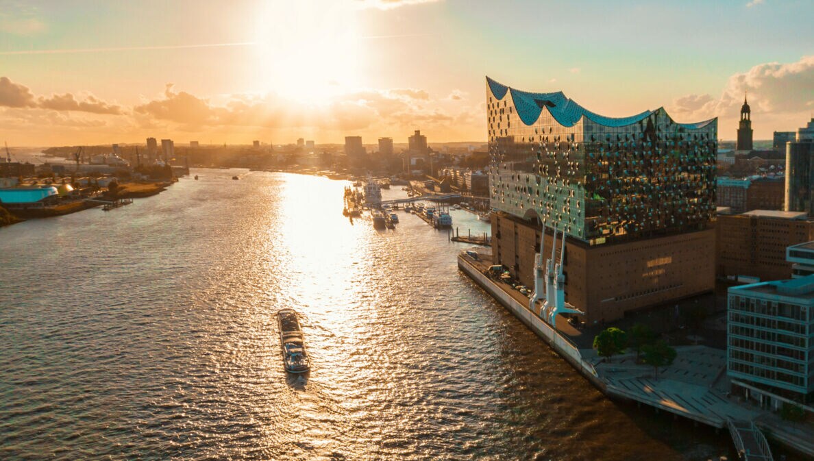 Sonnenuntergang über der Elbphilharmonie in Hamburg mit einem Schiff auf der Elbe und Stadtansicht im Hintergrund.