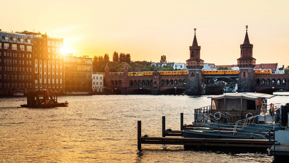 Sonnenuntergang über der Oberbaumbrücke in Berlin mit vorbeifahrender U-Bahn und Booten auf der Spree.
