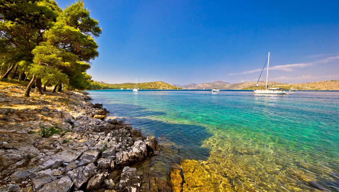 Bucht mit klarem Wasser und Booten umgeben von einer felsigen Landschaft mit Bäumen.
