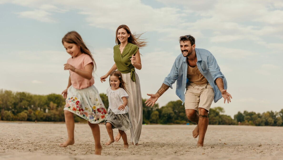 Familie mit zwei Kindern läuft barfuß am Strand bei bewölktem Himmel
