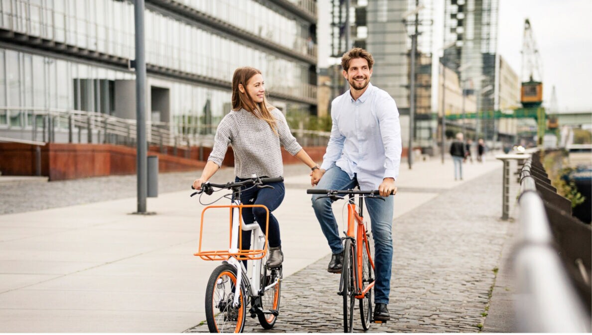 Paar hält Händchen beim Fahrradfahren auf einem gepflasterten Weg in einem modernen Stadtviertel