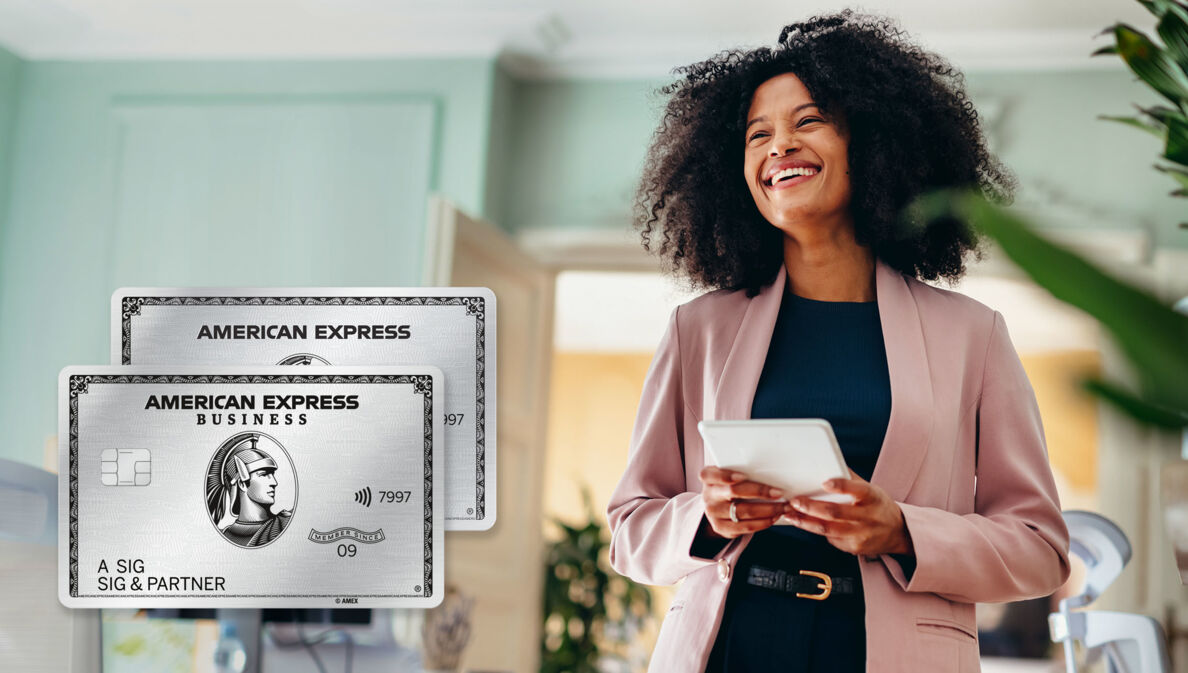 Eine lachende Frau in einem rosafarbenen Blazer steht in einem modernen Büro und hält ein weißes Tablet in den Händen, daneben ein Freisteller einer silbernen American Express Business Kreditkarte über einer einfachen American Express Platinum Card.