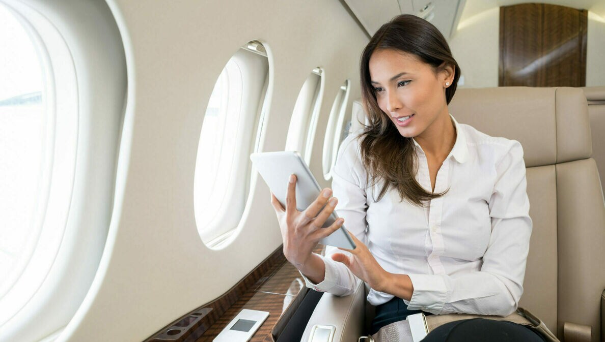Eine Geschäftsfrau sitzt im Flugzeug und arbeitet an ihrem Tablet.