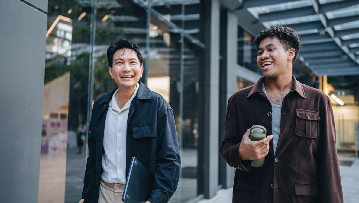 Zwei Kollegen spazieren gemeinsam und halten dabei eine Projektbesprechung ab.