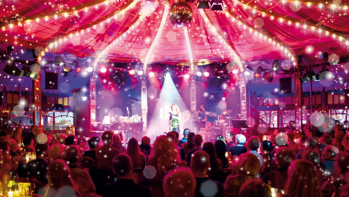 Bühne im Bar jeder Vernunft Theater Berlin mit Künstlerin im Scheinwerferlicht vor Publikum unter Zelt mit Lichterketten