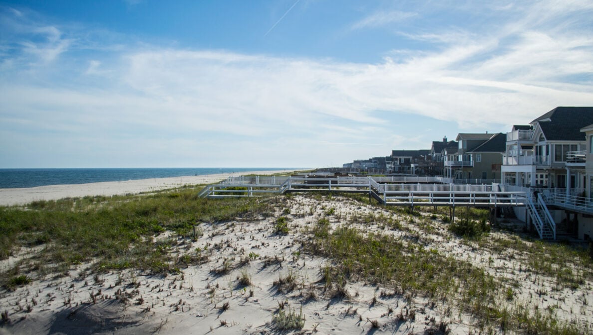 Weg zu einem Sandstrand mit Dünen unter blauem Himmel.