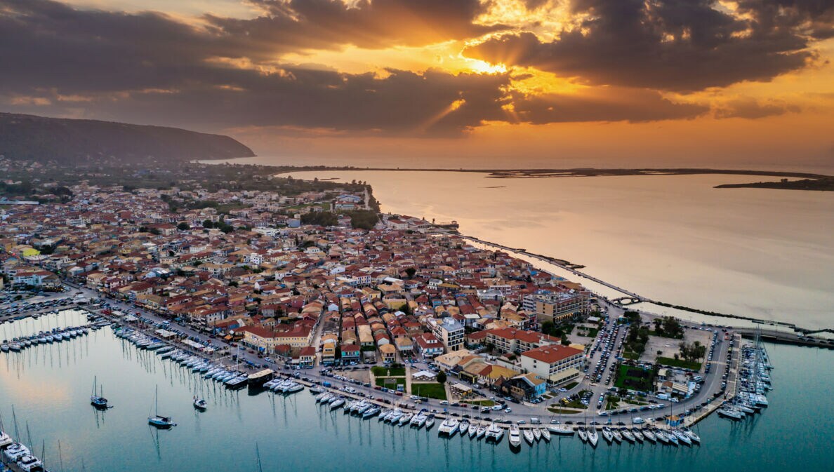 Küstenort mit Hafen von oben bei Sonnenuntergang umgeben von Meer.