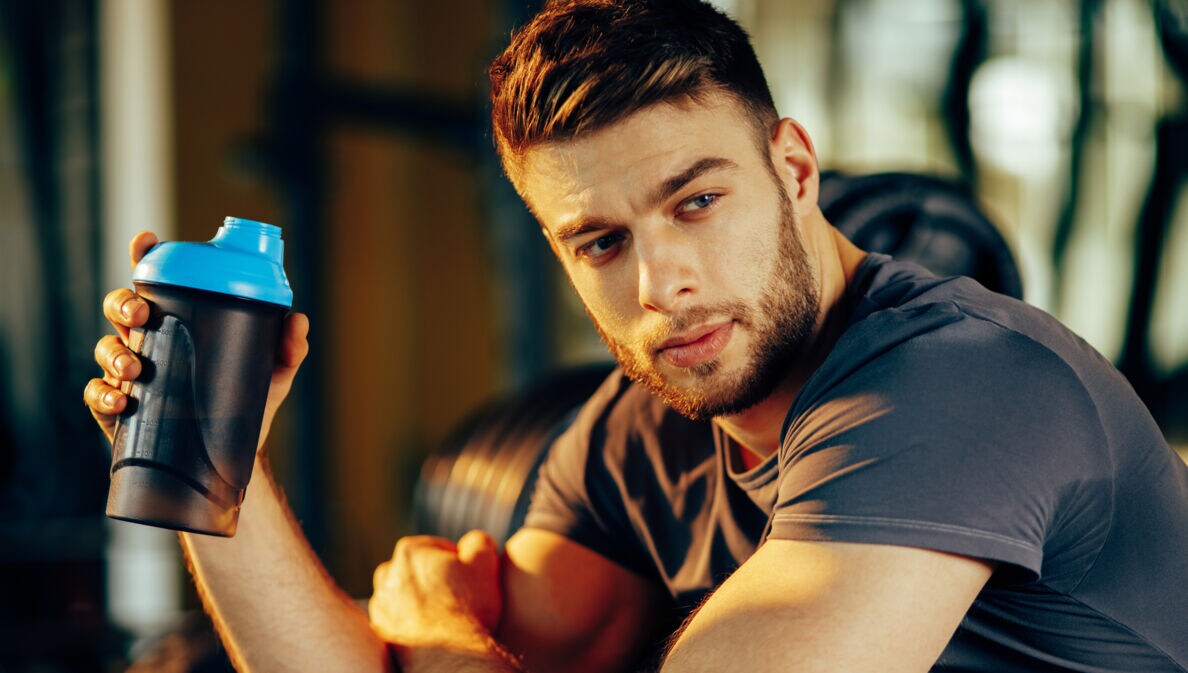 Ein Mann in Sportkleidung hält einen Protein-Shaker in der Hand.