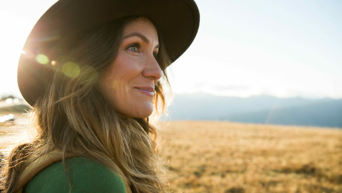 Eine junge Frau mit Hut schaut auf einer Wanderung in die Ferne