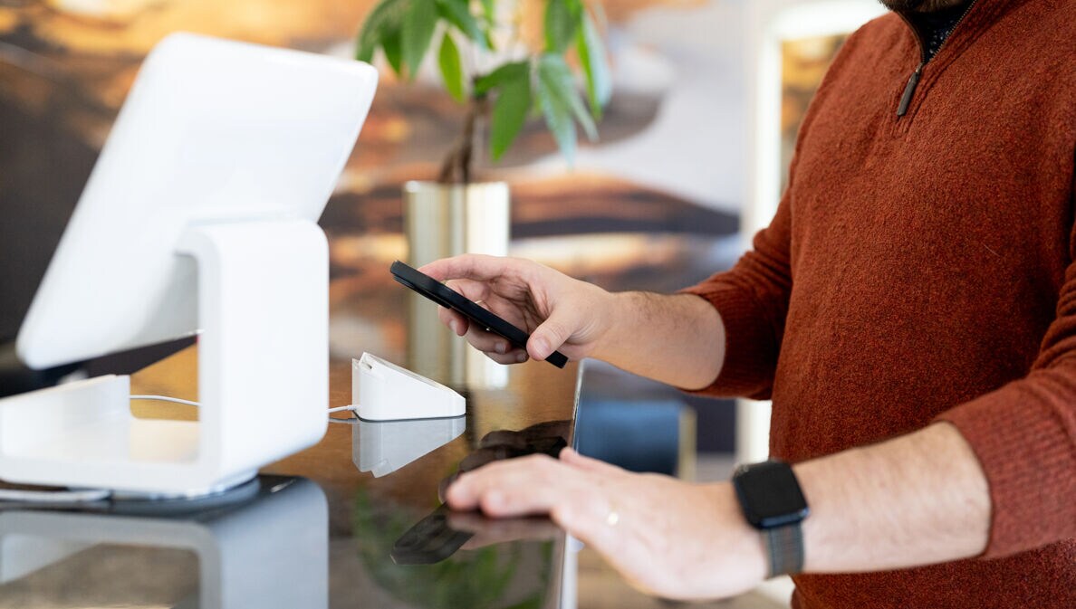 Nahaufnahme eines Mannes, der via Smartphone eine Zahlung in einem Geschäft tätigt.