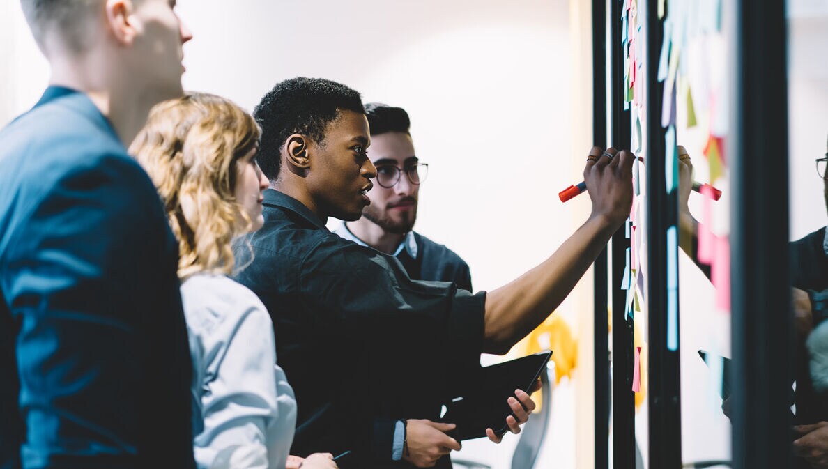 Eine Gruppe von Kolleg:innen steht am Whiteboard und erarbeitet in einem Workshop die Frage nach dem Warum.