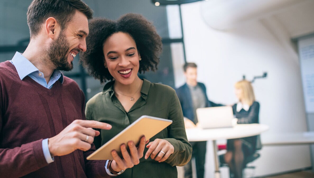 Zwei Kollegen stehen zusammen und schauen gemeinsam auf ein Tablet in einem Büro.