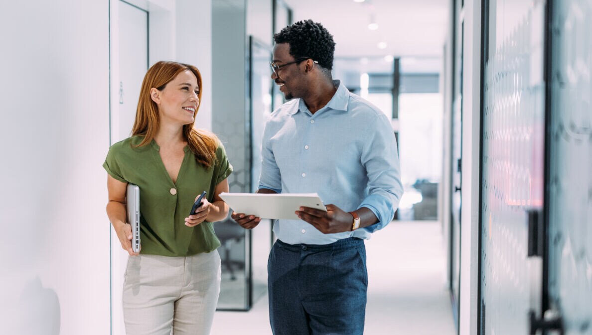Eine Frau und ein Mann mit Tablets in den Händen kommunizieren auf einem hellen Flur.