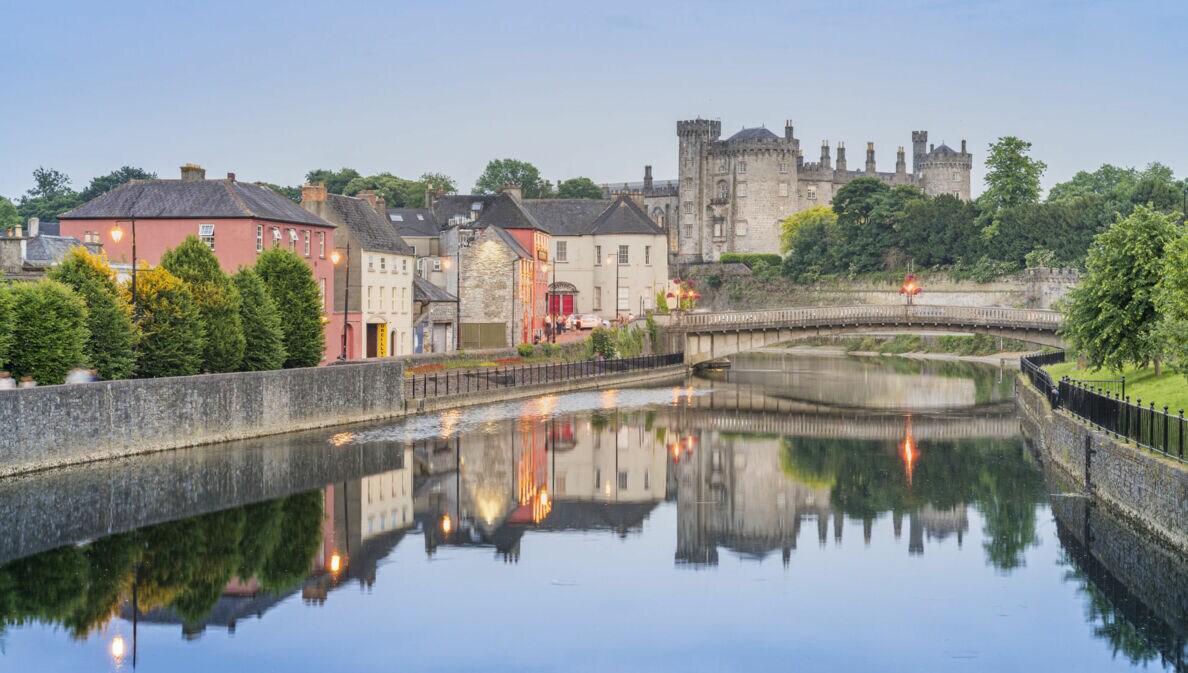 Blick auf Kilkenny mit Kilkenny Castle und der John’s Bridge vor dem Fluss Nore, indem sich die Lichter und Gebäude siegeln.
