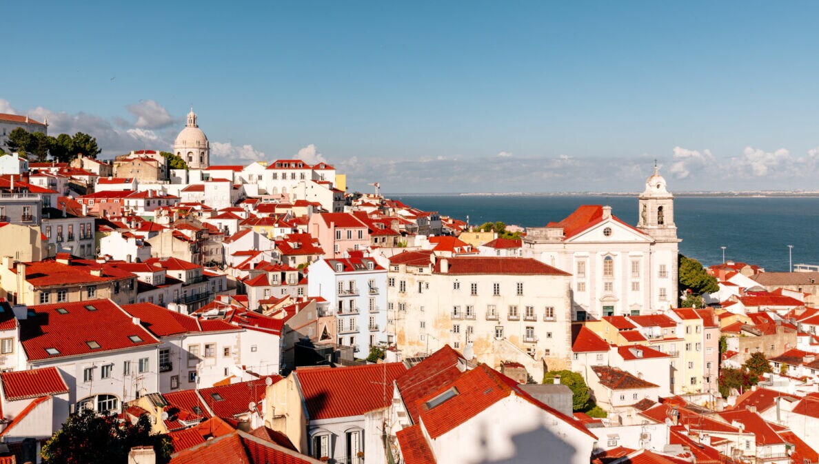 Blick auf die weißen Häuser mit ihren rotleuchtenden Dächern in Lissabons Altstadtviertel Alfama.