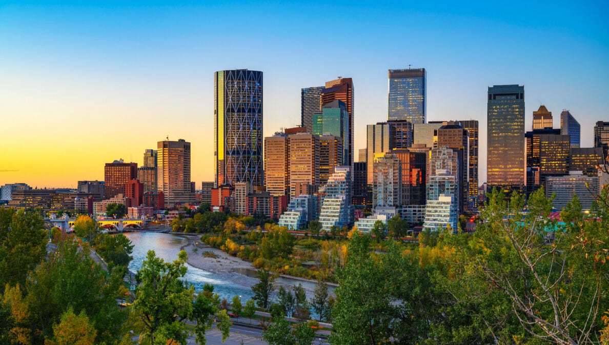 Sonnenuntergang über der Skyline der kanadischen Stadt Calgary, mit dem Bow River im Vordergrund.